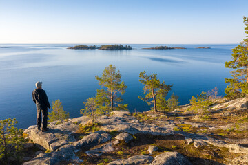 Fototapeta na wymiar A man on a rocky island with pine trees looks into the sea.