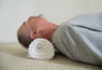 Senior citizen using a rolled up towel to treat neck pain