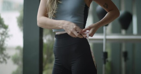 Close up shot of fit girl measuring her perfect waist in gym. Female athlete losing extra weight after keeping a diet and doing sports - motivation concept. 4k footage.