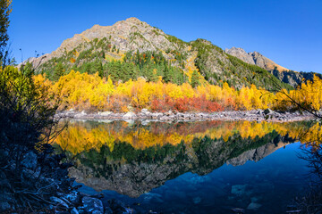 Beautiful autumn landscape with clear green water of a mountain lake and trees with autumn foliage reflected in it