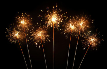 Fototapeta premium Sparklers sparkling on dark background. The golden sparks are scattered, creating a festive and celebratory atmosphere typical of joyous occasions like New Year's Eve, Fourth of July, or birthday