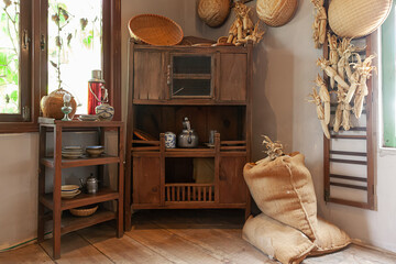 Interior of Vietnamese kitchen with porcelain vase, aluminum kettle, blue porcelain plate, rattan trivet coaster, oil lamp, vintage thermos bottle in a old wooden shelf