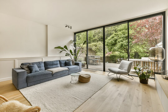 a living room with wood flooring and large windows looking out onto the trees in the backyard area is bright