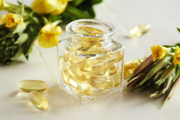 Obraz na płótnie Canvas Gel capsules of evening primrose oil in a bottle with fresh blooming plant