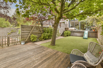 a backyard area with wooden decking and green grass in the yard is surrounded by trees, shrubs and flowers