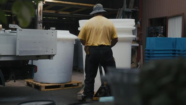 Male worker moving a huge white plastic liquid container on a Steel Dolly for Overpack