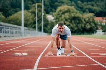 Obraz premium Young adult running on a track surrounded by lush, leafy trees in the background