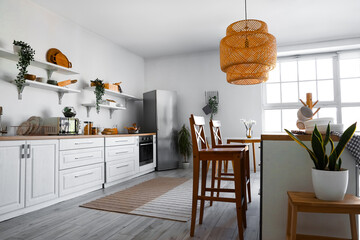 Interior of light kitchen with stylish fridge, counters, shelves, chairs and lamp