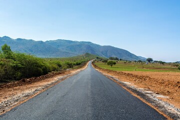 Desolate and empty asphalt road with bushes and a mountain range near Mysore, India.