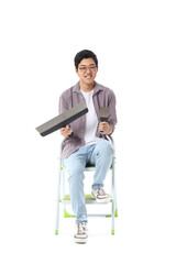 Young Asian man with putty knives sitting on white background