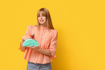 Female student with pencil case on yellow background