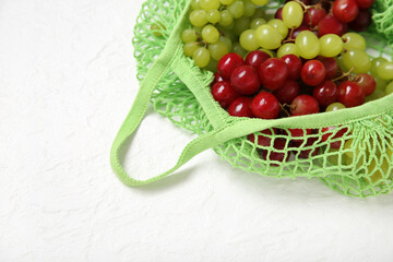 Mesh bag with different fresh grapes on white background, closeup