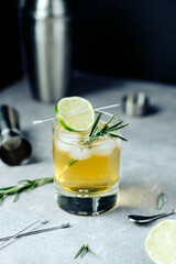 Alcohol cocktail with lime slice rosemary ice and cocktail shaker jigger on black background. Party time