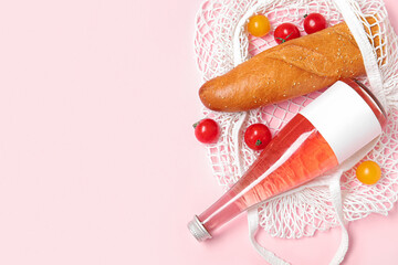 Mesh bag with fresh tomatoes, baguette and bottle of juice on pink background, closeup