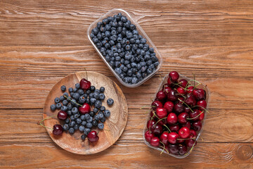 Plastic containers with fresh blueberry and cherry on wooden background