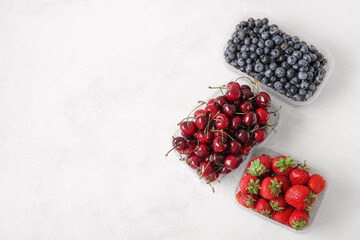 Plastic containers with fresh blueberry, cherry and strawberry on light background