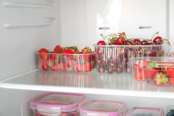 Plastic containers with fresh berries in refrigerator