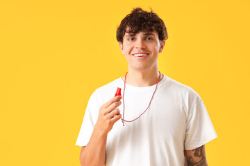 Male lifeguard with whistle on yellow background