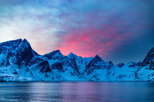 Snowy mountains near sea against cloudy sky at sunset