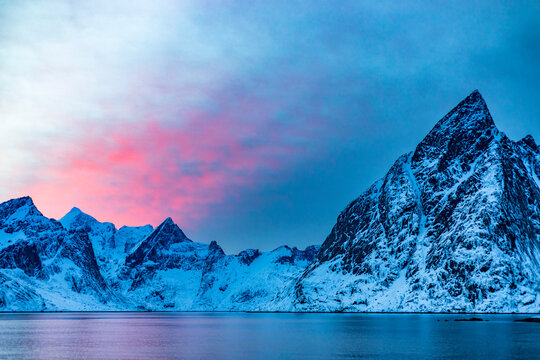 Snowy mountains near sea against cloudy sky at sunset