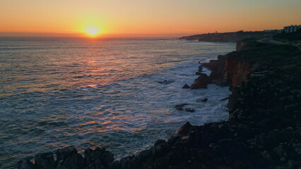 Golden sunset foaming ocean water splashing on rough rocky coastline aerial view