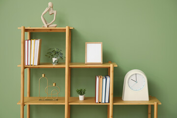 Shelving unit with books, clock and blank frame near green wall in room