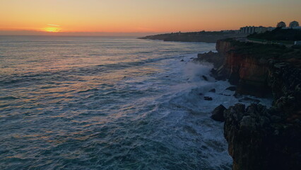 Fototapeta na wymiar Beautiful calm coastal sunset over foamy ocean splashing on rocky shore aerial