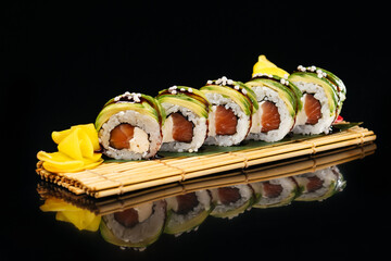 Green Dragon sushi with eel, tobiko caviar, cream cheese, cucumber, avocado, unagi sauce, sesame on a green leaf, which is located on a board made of wooden sticks tied with string on a black backgrou