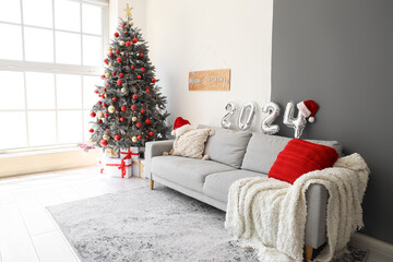 Balloons in shape of figure 2024 on grey sofa in living room with Christmas decor