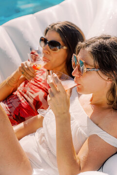 two women float in pool sipping drinks