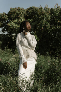 Young black model standing in field in stylish white outfit