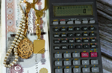 A calculator, silver rosary and gold keyring medals with a text Allahu Akbar, translation (God is...