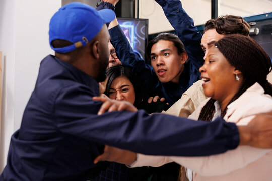 African man security guard pushing back crazy obsessed customers at shop entrance during Black Friday sale. Crowd of anxious diverse people shoppers breaking into shopping mall on Cyber Monday