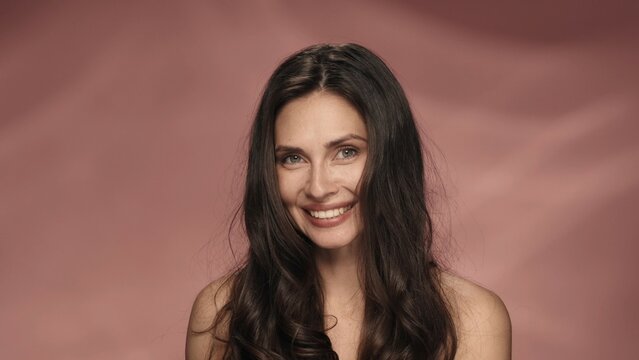 Portrait of a seminude woman on a pink background close up. Longhaired brunette woman with a charming smile. Beauty concept. Natural beauty, cosmetology, skin care.