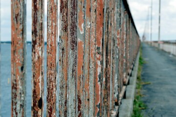 Aged, rusted wall situated next to a body of water, with a concrete pathway running between them