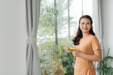 pretty asian woman with cup of hot drink, at home window