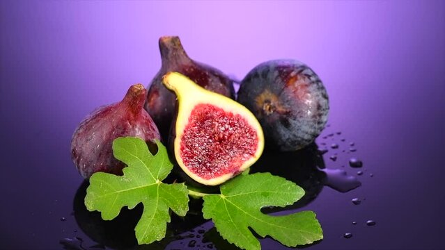 Fig fruits. Ripe sweet figs fruit with leaves close up, on purple, violet background. Water drops. Rotating fresh exotic fruits. Slow motion