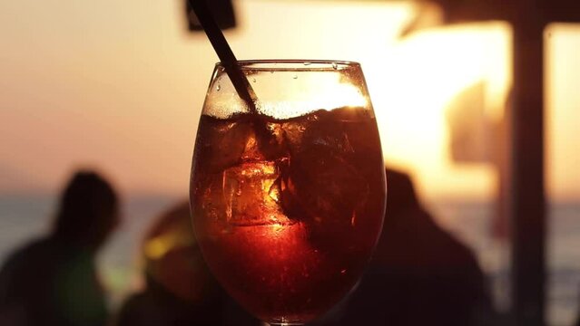 Closeup of an iced cocktail in a glass with sunset shining in the background at a beautiful beach