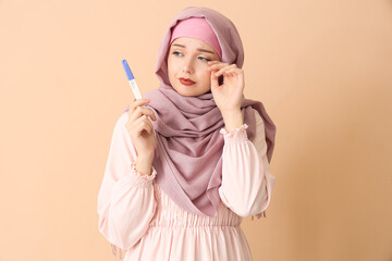 Worried Muslim young woman with pregnancy test on beige background