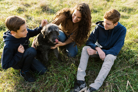 smiling family with teenagers petting their dog outdoors in a field