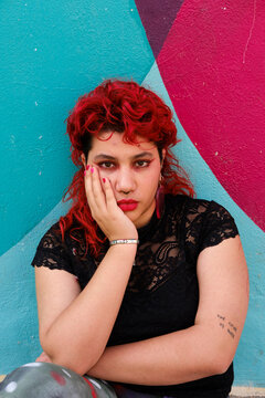 Red hair queer person posing in front of colorful wall 