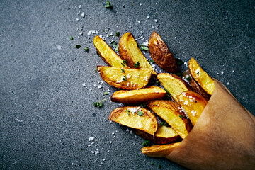 Potato wedges with sea salt and herbs in a paper bag