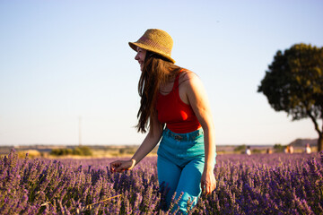 A beautiful cheerful young woman wearing straw hat in blooming lilac lavender field. Female...