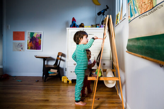 siblings stand at easel and paint together