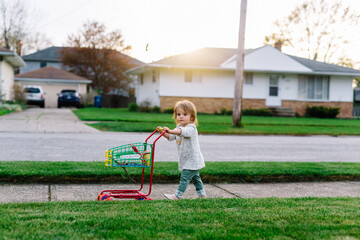 Little girl pushes toy shopping card down sidewalk