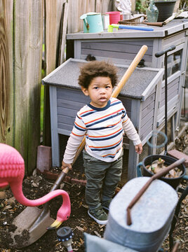 A toddler boy in a garden holding a shovel