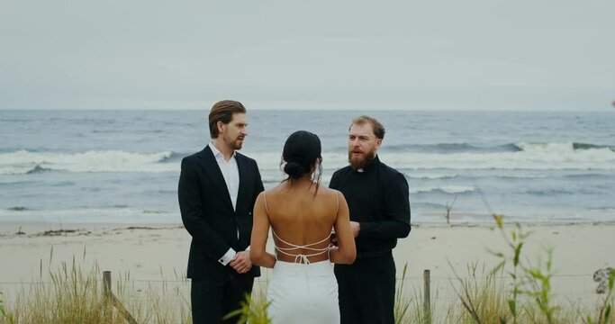 The wedding of a young couple on the seashore, the priest says a speech