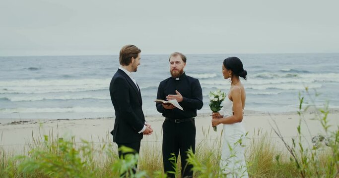 The wedding of a young couple on the seashore, the priest says a speech