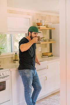 Millennial bearded man in kitchen, sipping a cup of coffee