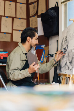 A Latino man makes a painting in his small studio at home.